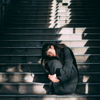 階段に蹲る黒いコートの女性、膝を抱えて思い詰めた表情の写真