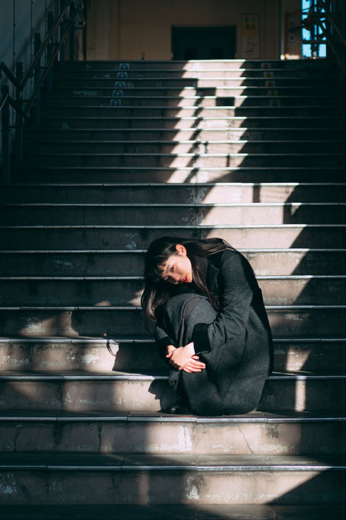 階段に蹲る黒いコートの女性、膝を抱えて思い詰めた表情