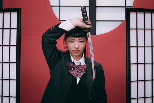 緑色の学生服姿の女子高生と日本刀を構えた和風コスプレ