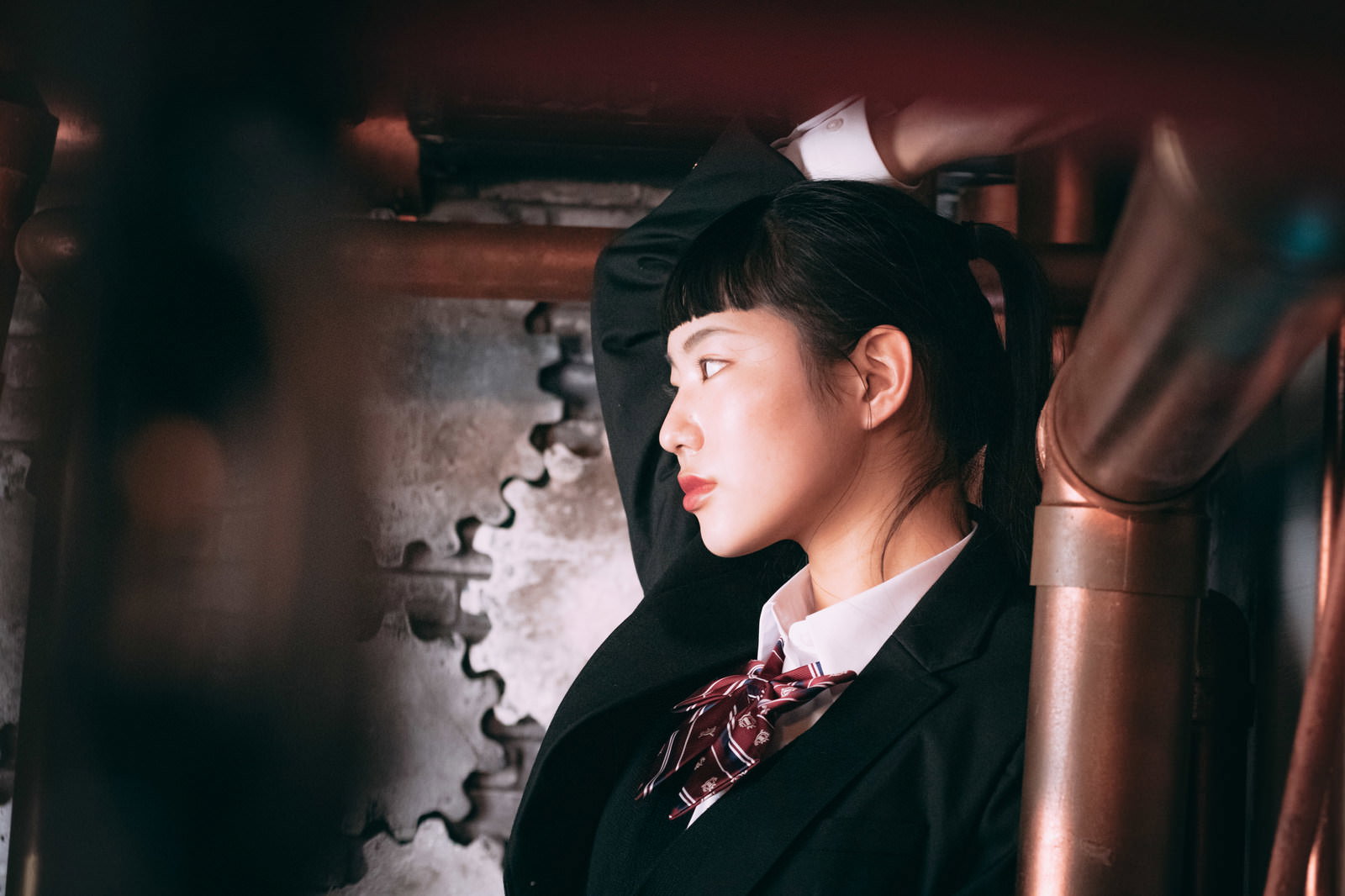 黒いスーツとネクタイ姿で、オン眉のポニーテールをした女性の横顔［モデル：なんこ］