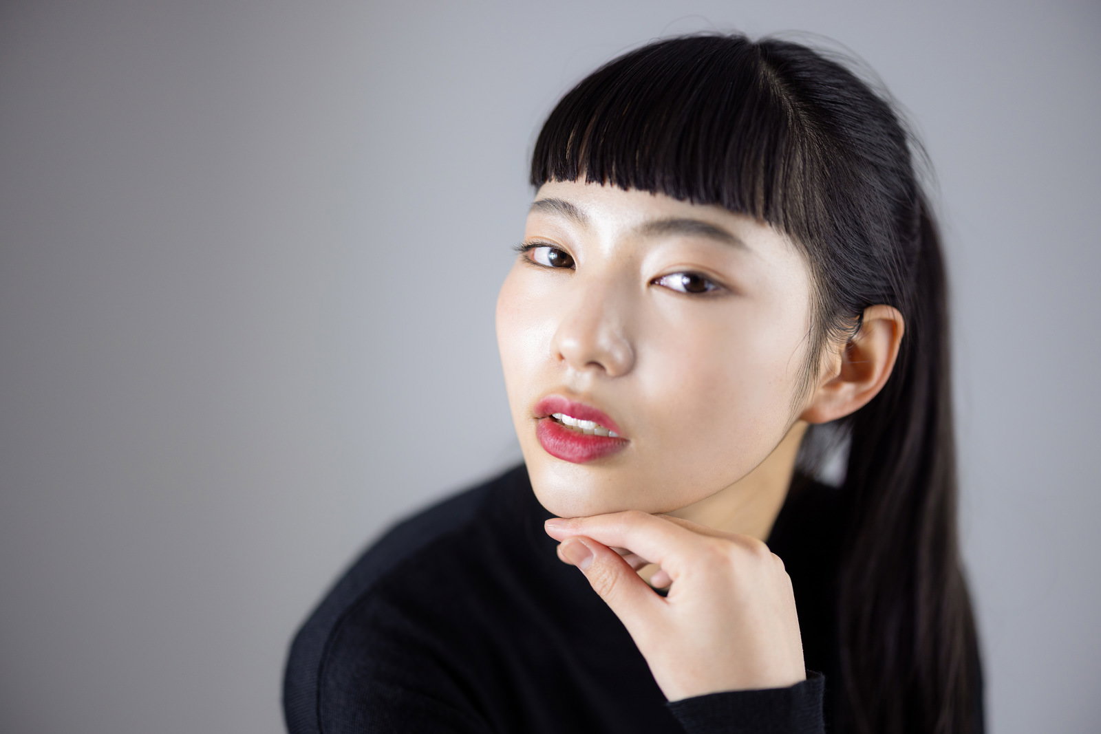 黒い前髪のオン眉ヘアで頬杖をついてすまし顔の女性［モデル：なんこ］