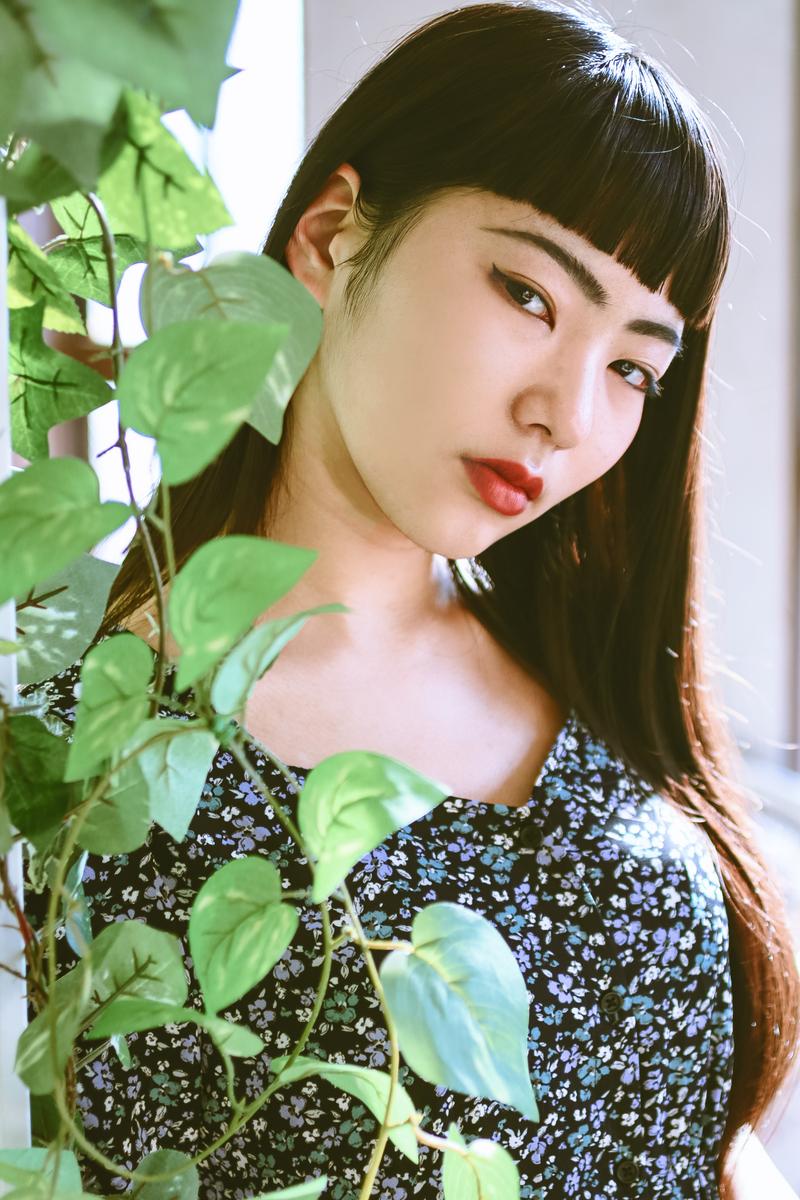 観葉植物の枝越しにポーズを取る黒髪の女性［モデル：なんこ］