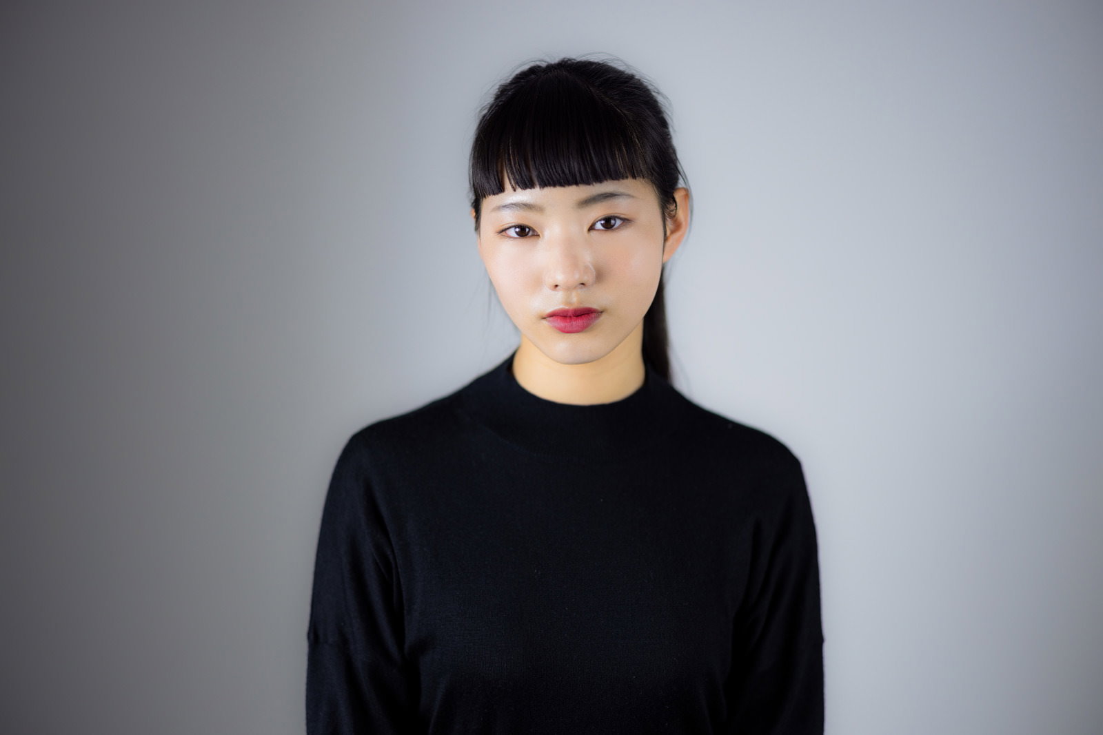 黒いタートルネック姿でオン眉の真顔でポージングする女性［モデル：なんこ］