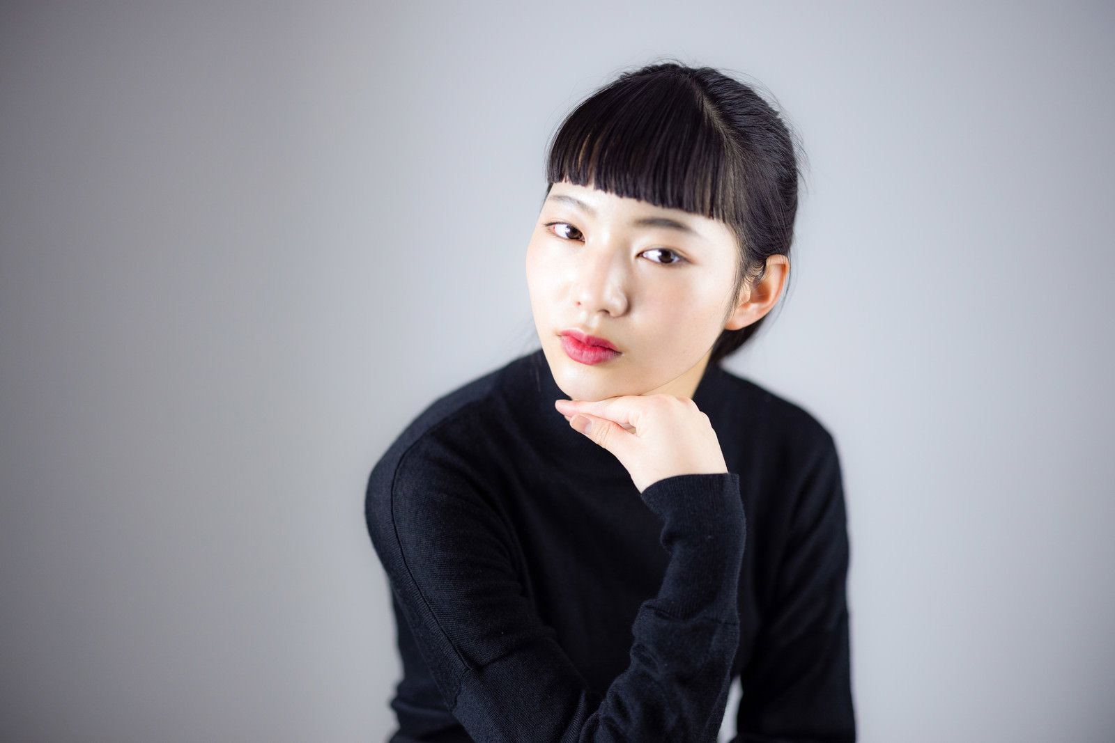 頬杖をついて澄ました表情をする黒いセーター姿の女性［モデル：なんこ］