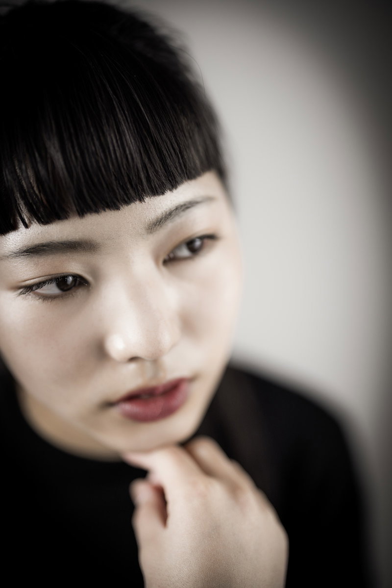 頬杖をついて斜め下を見つめるツンとした表情の女性［モデル：なんこ］