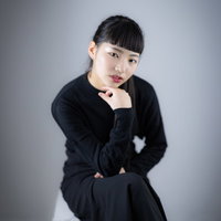 黒いブラウスで足を組んで頬杖をつく女性のプロフィールの写真
