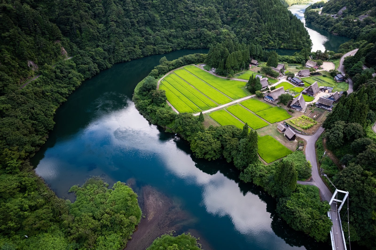 山間部の菅沼集落を空撮した風景、合掌造りの建物と蛇行する庄川