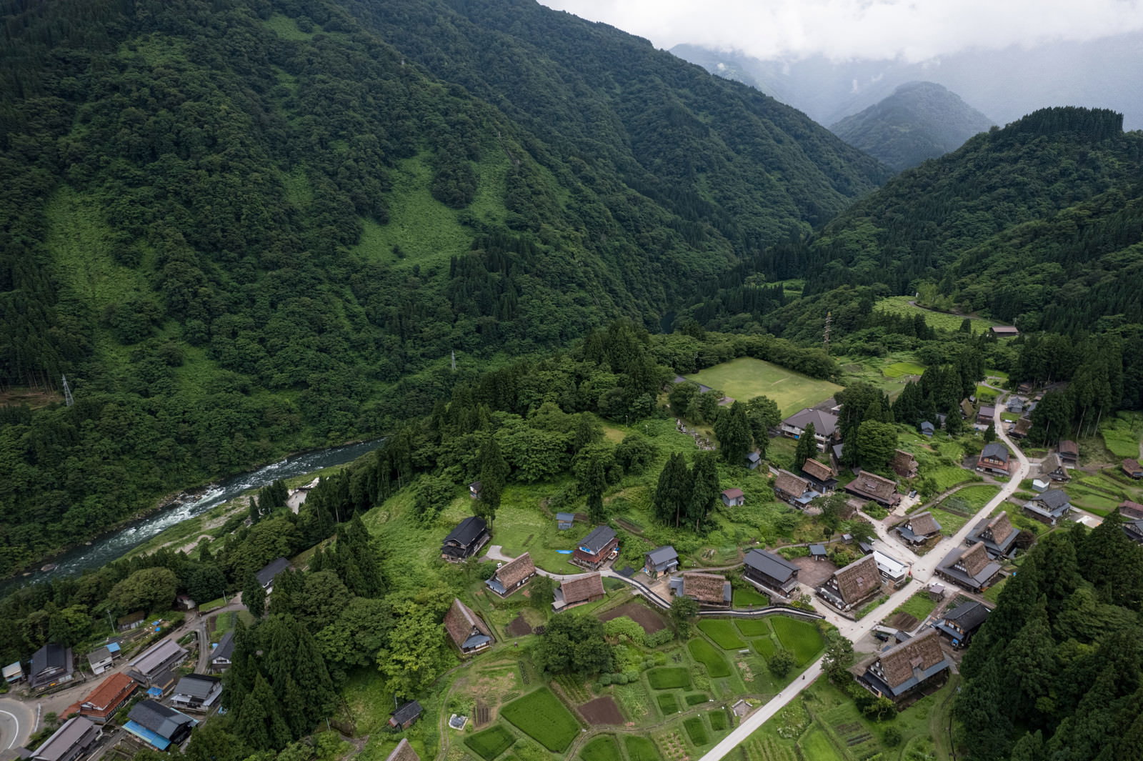 緑の山々に囲まれた谷間に点在する相倉合掌造り集落の空撮写真
