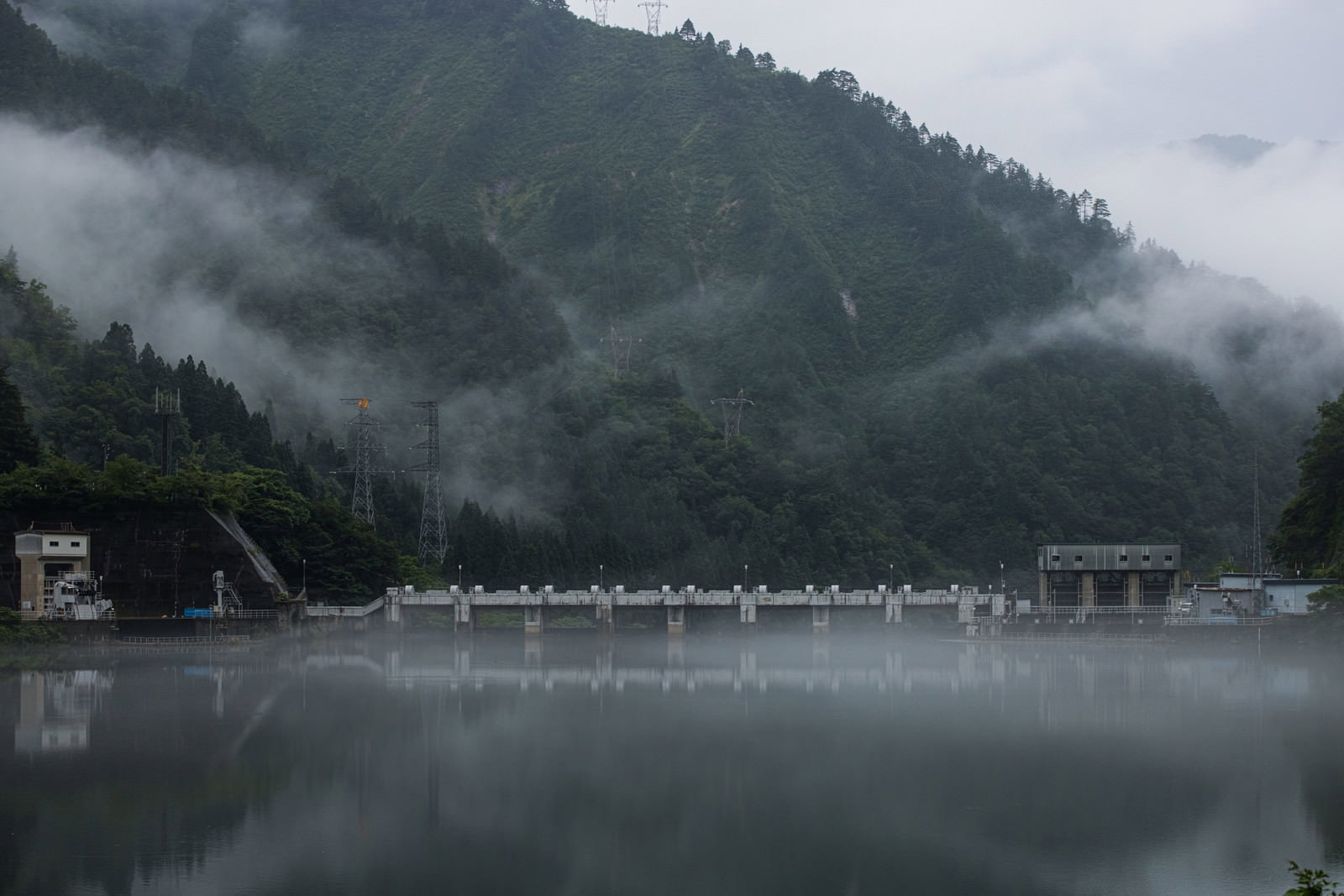 霧に包まれたダム湖の風景、静寂な水面に山の緑が反射している
