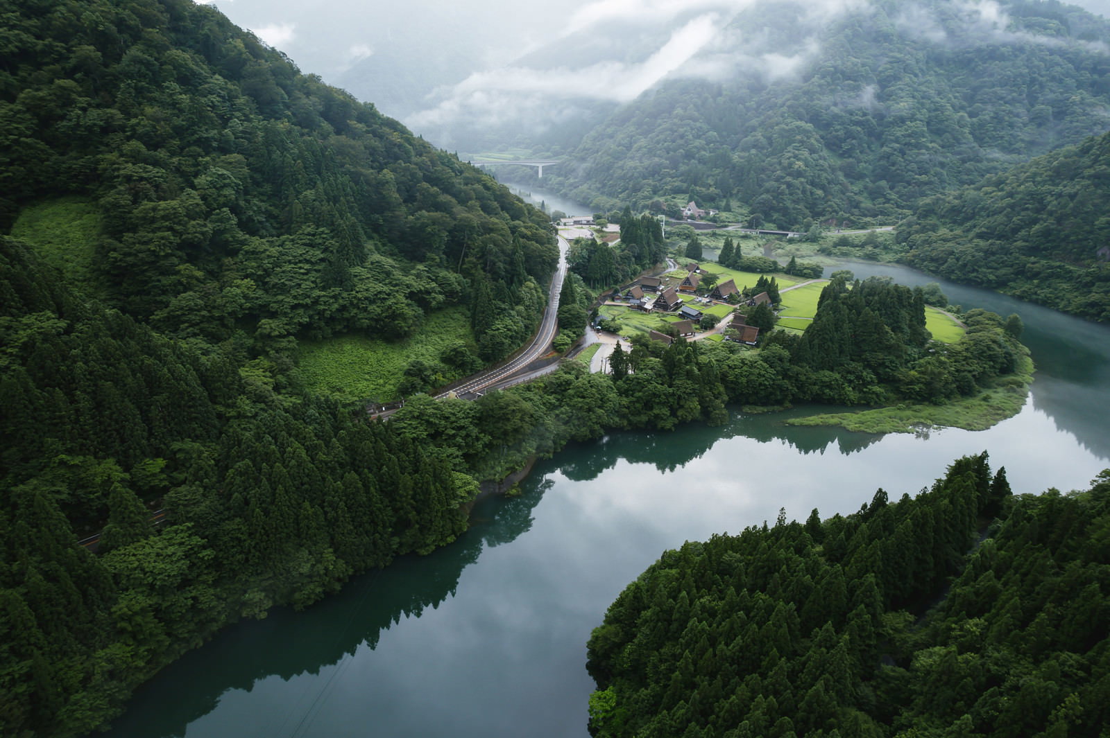 山間の川沿いに点在する茅葺屋根の合掌造り集落を空撮で捉えた風景