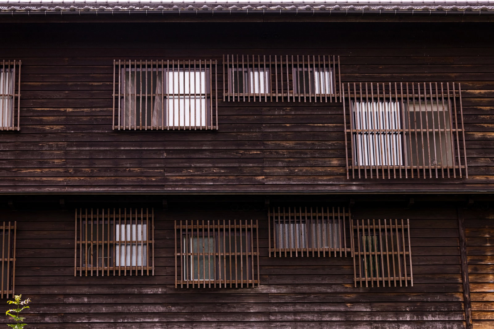 茶色い木造建築の外壁に格子窓が並ぶ伝統的な日本家屋