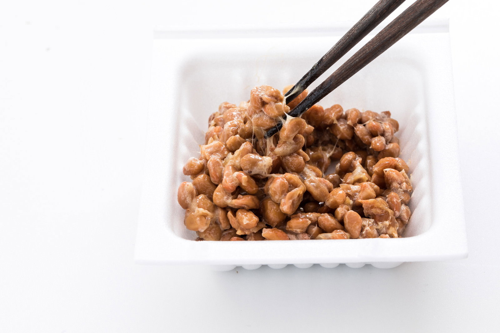 白いパックに入った納豆を黒い箸でかき混ぜている様子