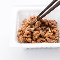 パックに入った納豆を箸でかき混ぜる、白いパックで粘り気を出す様子の写真