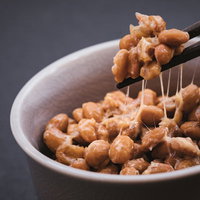 白い器の丸大豆納豆を箸で持ち上げた糸引きの写真