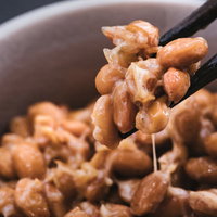 納豆をかき混ぜないで箸でつまんで食べる朝食のご飯のおかずの写真