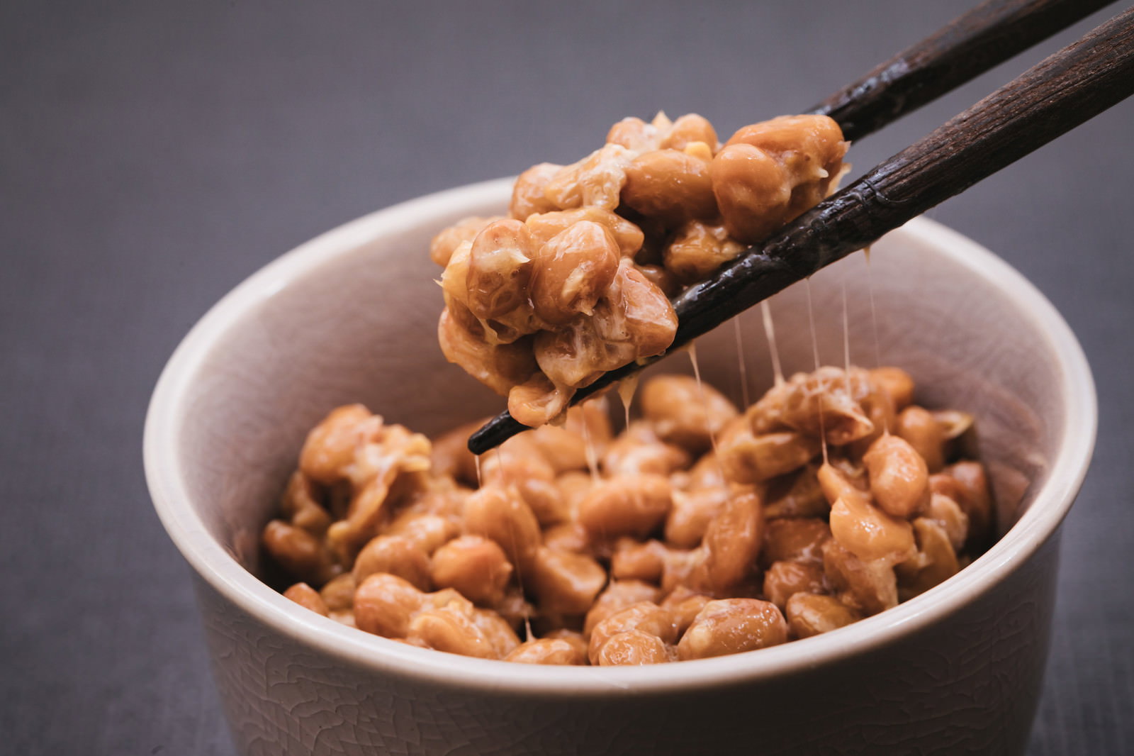 茶碗に盛られた納豆を箸でつまみ上げ、糸を引いている様子