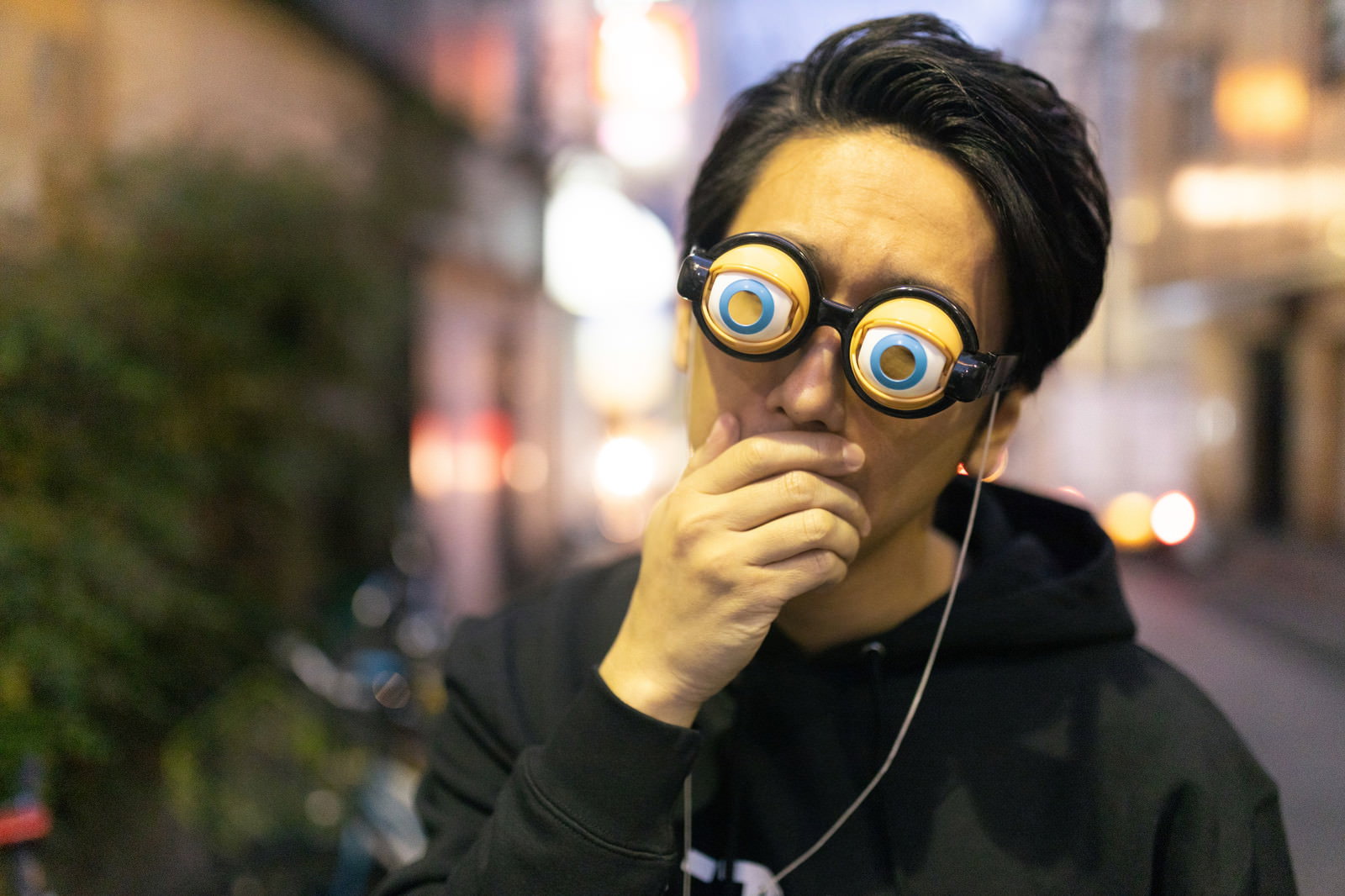 大きな丸眼鏡をかけて口元を手で覆い驚愕の表情を浮かべる男性［モデル：大川竜弥］