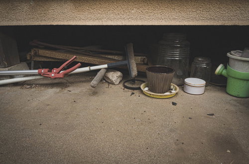 廃屋の民家の軒下に並ぶ園芸用の鉢とプランター