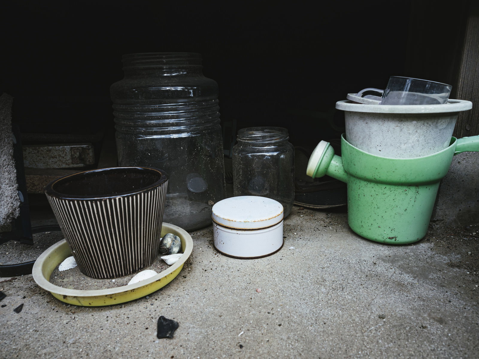 軒下のコンクリート床に放置された複数の鉢植えとプランター