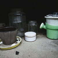 廃屋の軒下に放置された古い鉢植えと劣化したプランターの写真