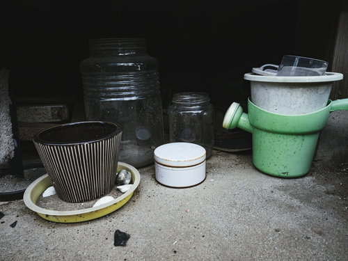 廃屋の軒下に放置された古い鉢植えと劣化したプランター