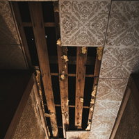 天井が剥がれ落ちた廃屋の室内、露出した木材の梁と老朽化した壁の写真