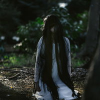 樹海の薄暗い森で座り込む白衣の女性の写真