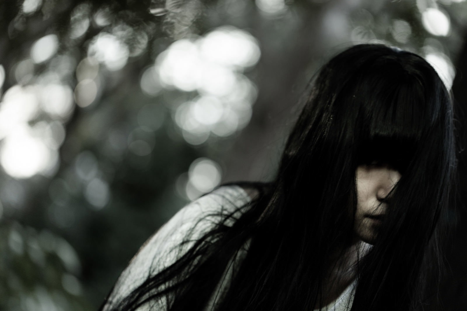 長い黒髪で顔を隠した女性の怨霊が薄暗い背景に佇んでいる［モデル：緋真煉］