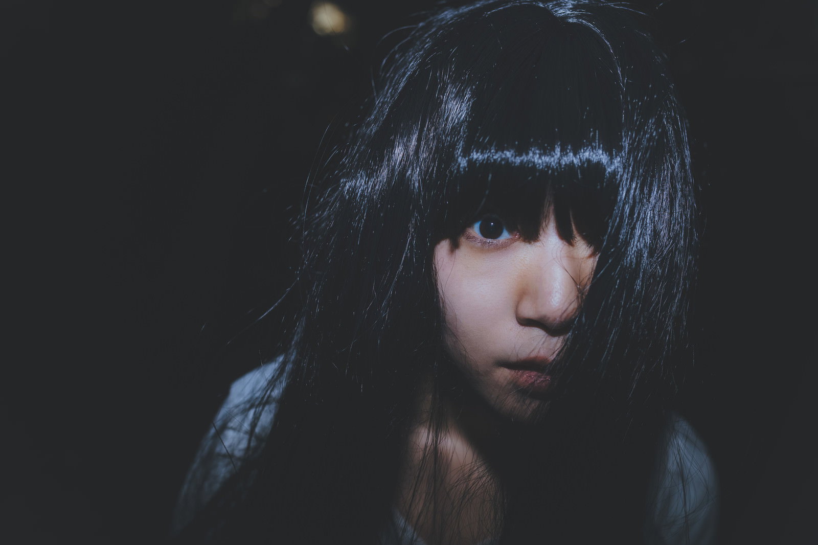 暗闇の中で黒髪の女性が静かに佇んでいる様子［モデル：緋真煉］