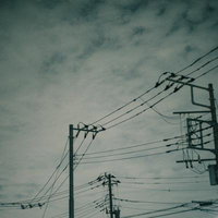 雲行き怪しい空に立つ複数の電柱と電線が張り巡らされた風景の写真