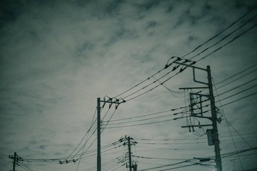雲行き怪しい空に立つ複数の電柱と電線が張り巡らされた風景