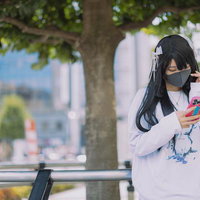待ち合わせで駅前の柵に座りスマホを見るマスク女子の写真