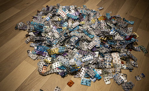 木目の床に散らばった大量の錠剤とカプセル