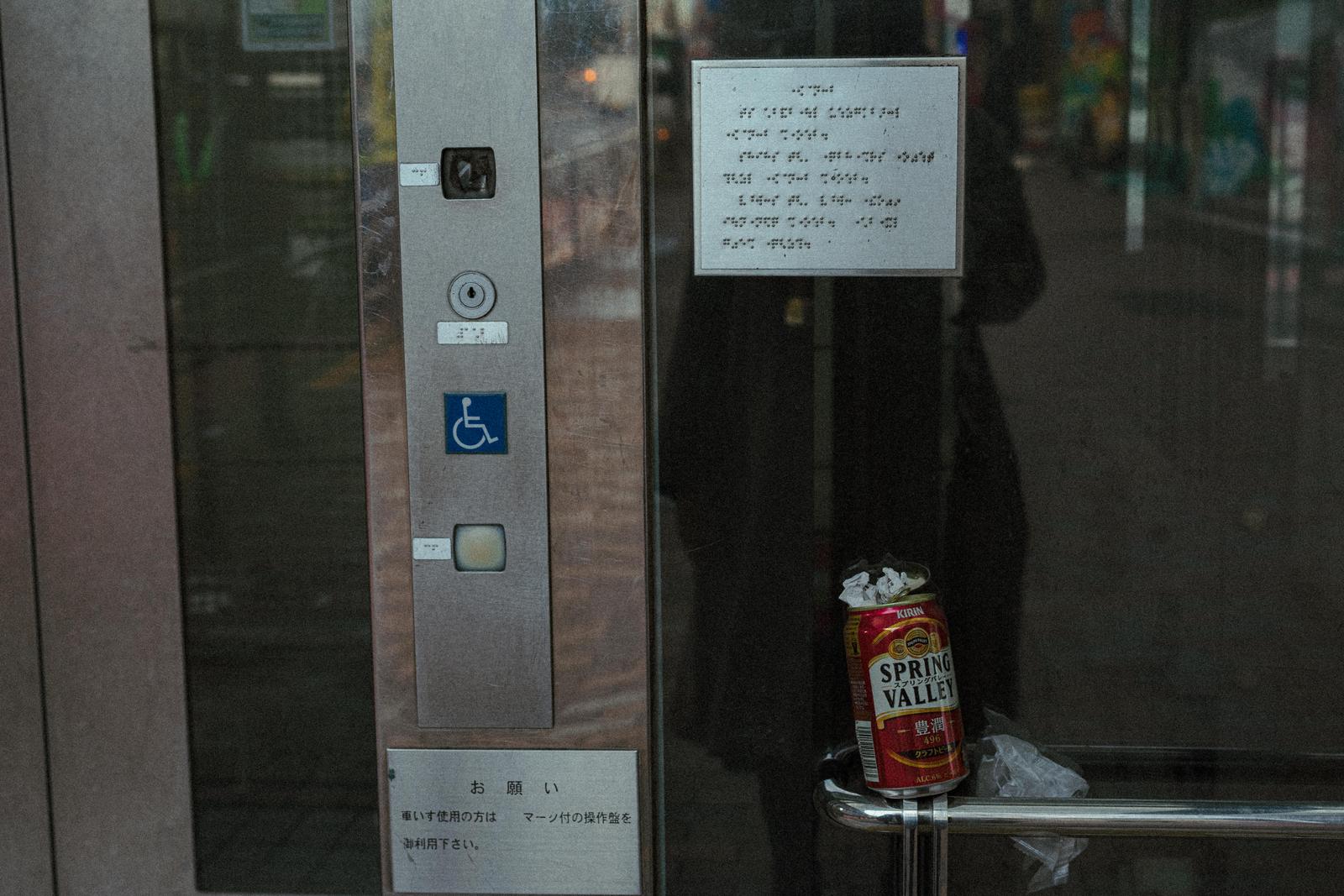 An empty can placed on the handrail with a braille display in front of the elevator