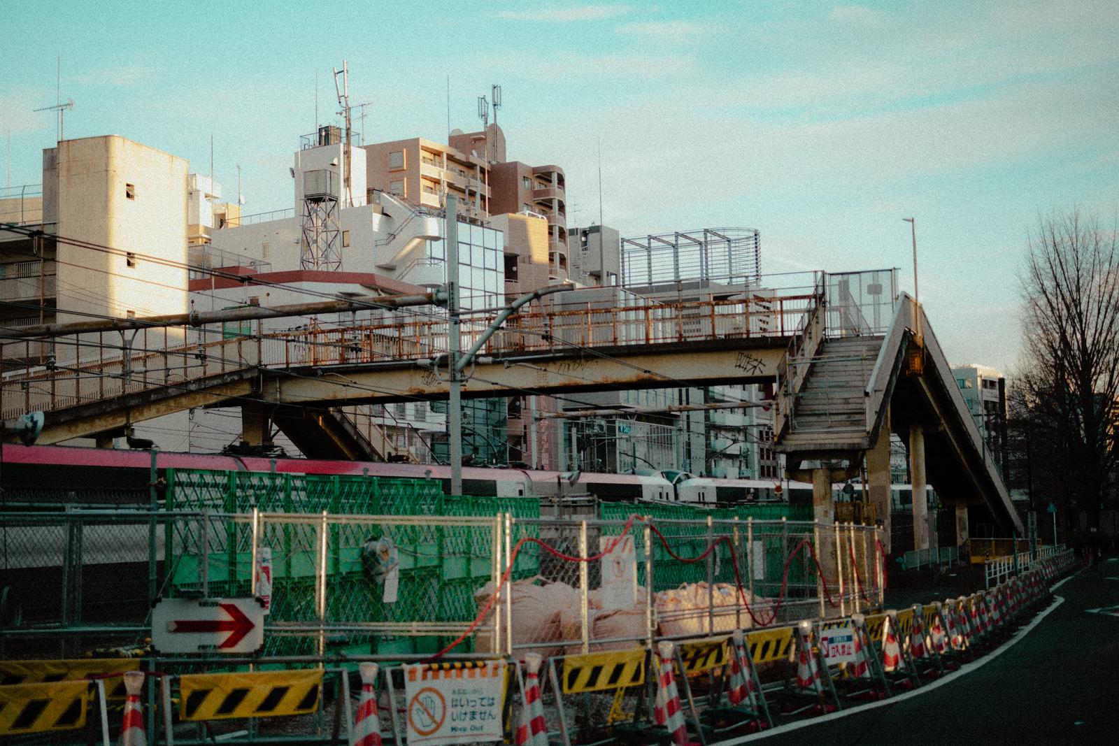 緑のフェンスで囲まれた工事現場と背景に見える高架歩道橋