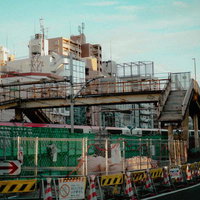 緑のフェンスに囲まれた再開発工事現場と古い高架歩道橋（渋谷）の写真