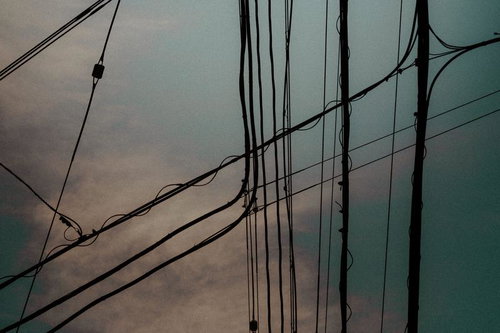 夕暮れの空に描かれる交差する電線と柱のシルエット