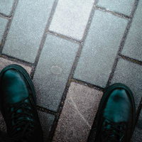 濡れた歩道に映る黒い革ブーツの足音と石畳の質感の写真