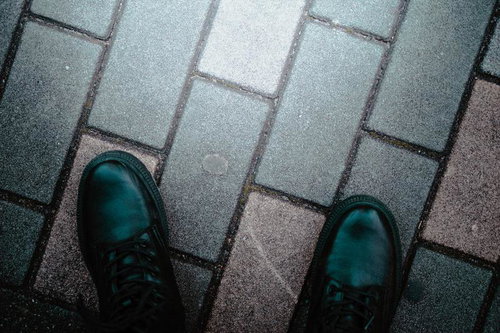 濡れた歩道に映る黒い革ブーツの足音と石畳の質感