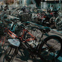 アスファルト駐輪場に並ぶ赤と黒の自転車群の写真