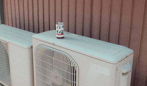 室外機の上に置かれたメッセージ缶とベージュのカーテン