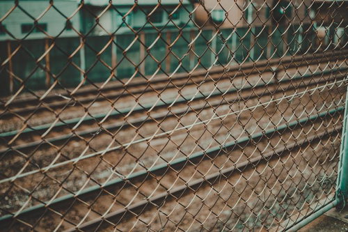 金網越しに見るJR総務線の電車と線路、駅構内の停車風景