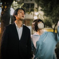 夜間の繁華街を歩くスーツ姿の男性とマスク女子の写真