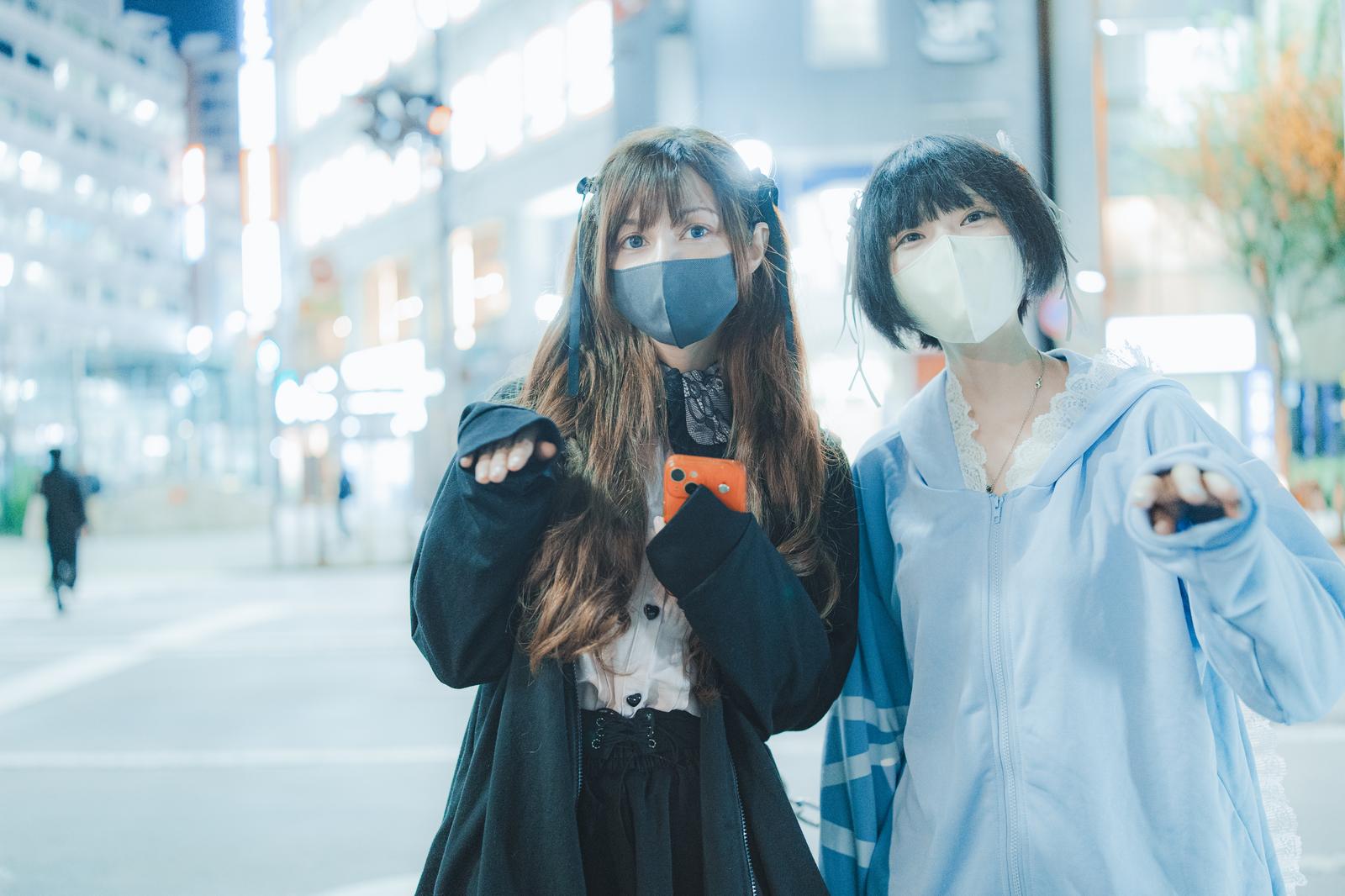 マスクをした黒髪女性が都会の繁華街で客引きをしている［モデル：ラミエル 緋真煉］