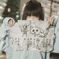 水色パーカーを着た黒髪の女の子が怪文書を掲げる姿の写真