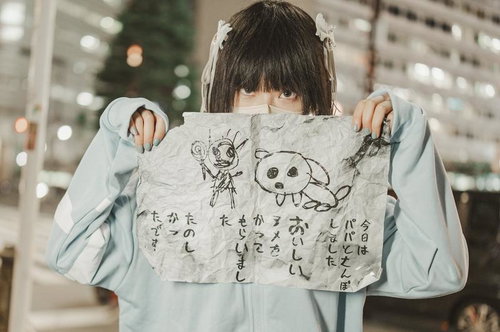 水色パーカーを着た黒髪の女の子が怪文書を掲げる姿