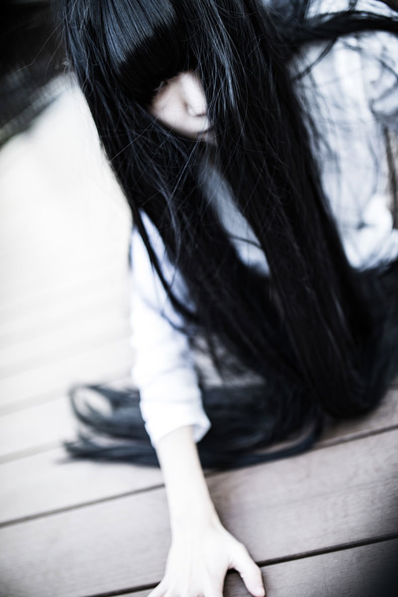 長い黒髪で顔を隠し白い服を着て床に座る女性［モデル：緋真煉］