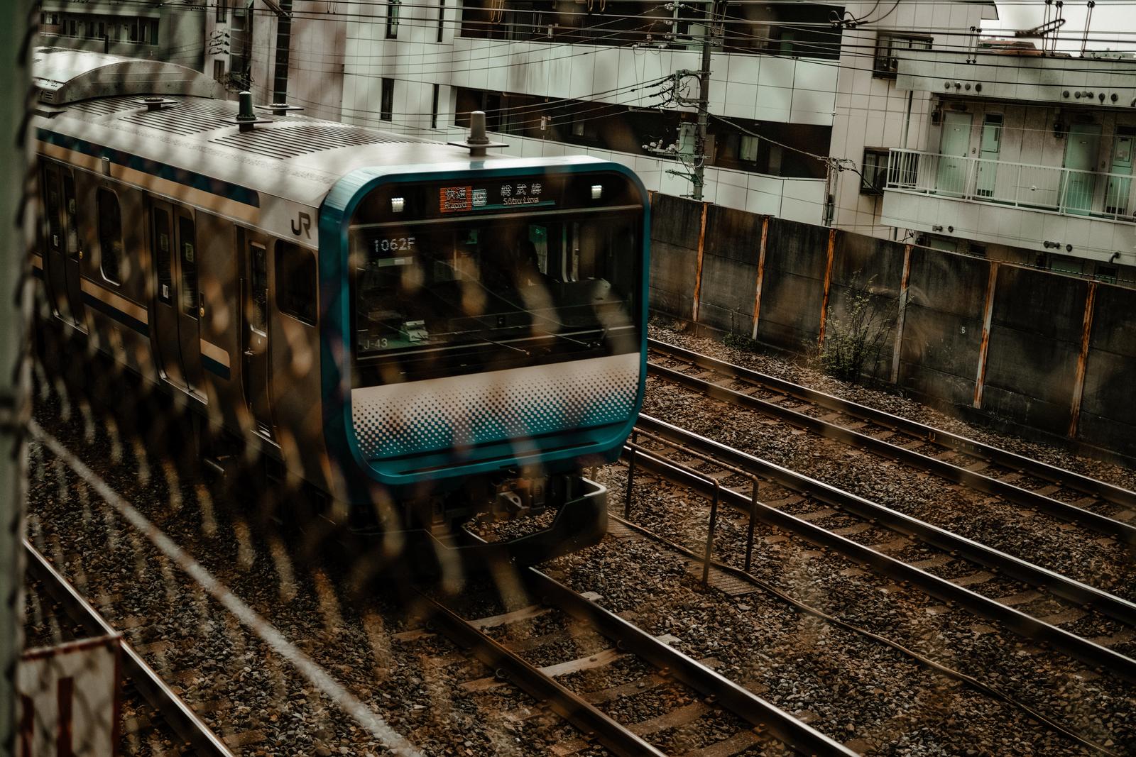 金網越しに走るJR総武線の電車