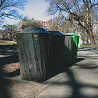 公園の歩道脇に設置された緑色のゴミ箱の写真