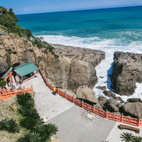 絶壁に囲まれた岩窟の鵜戸神宮の朱色の社殿と参拝風景の写真